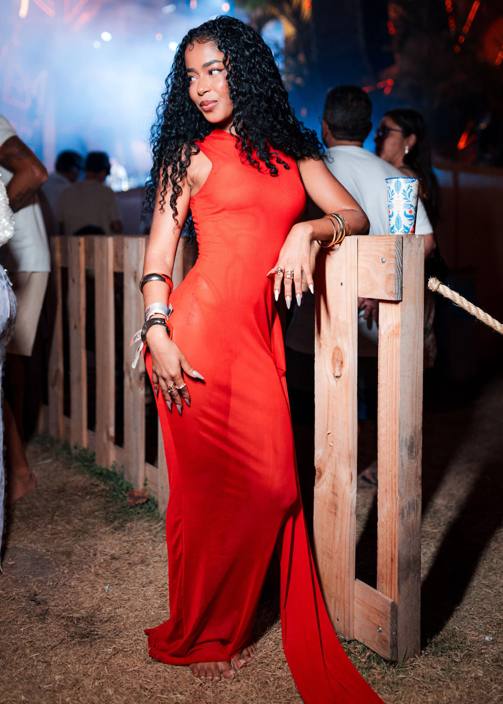 Modelo posa com vestido longo vermelho justo de tecido fluido, destacando acessórios em prata e clima elegante e confiante.