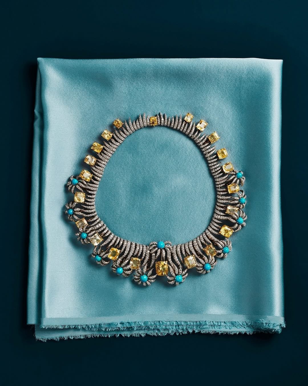 Colar sofisticado com pedras amarelas e turquesas sobre tecido azul acetinado destaca luxo e inovação na indústria da moda