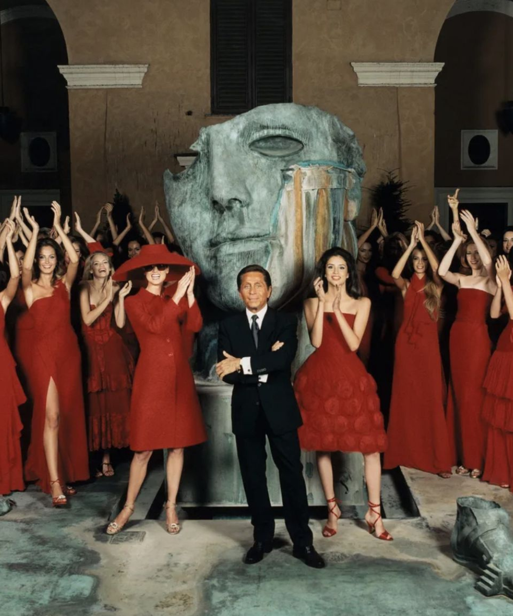 Valentino posa ao centro com modelos em vestidos e casacos vermelhos vibrantes, texturas fluidas e estruturadas, celebrando