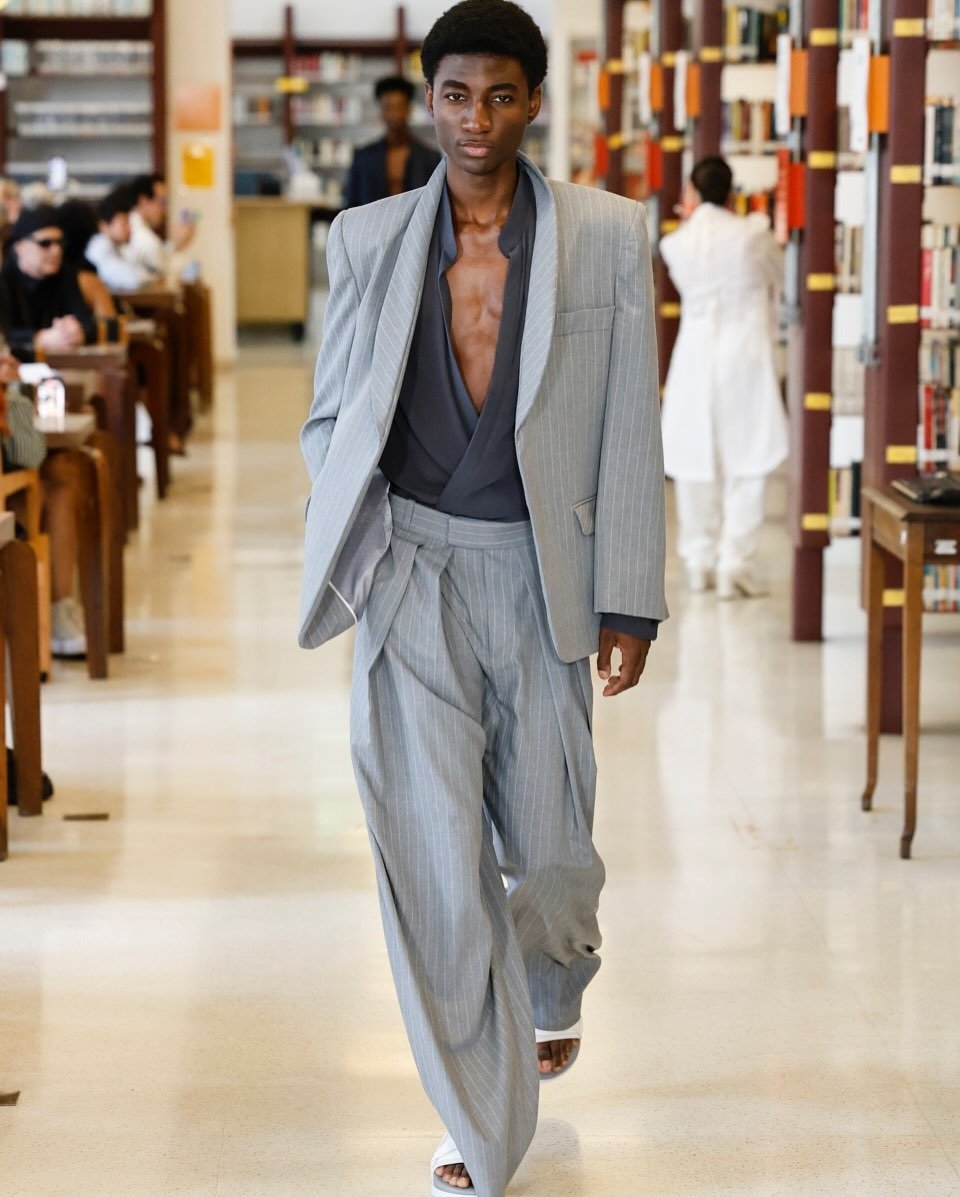 Wagner Moura no Oscar com terno cinza claro listrado oversized, camisa preta aberta e calça ampla, exalando elegância