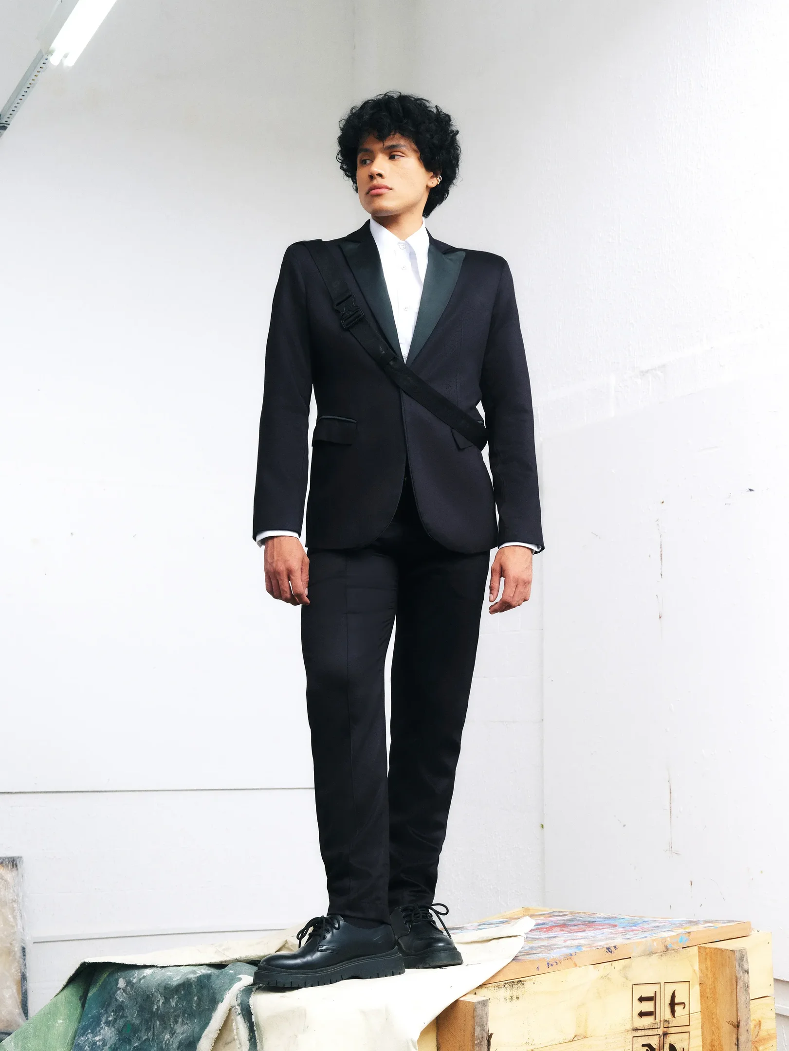 Wagner Moura no Oscar. Terno preto slim com blazer de lapela acetinada, camisa branca e sapatos pretos, posando