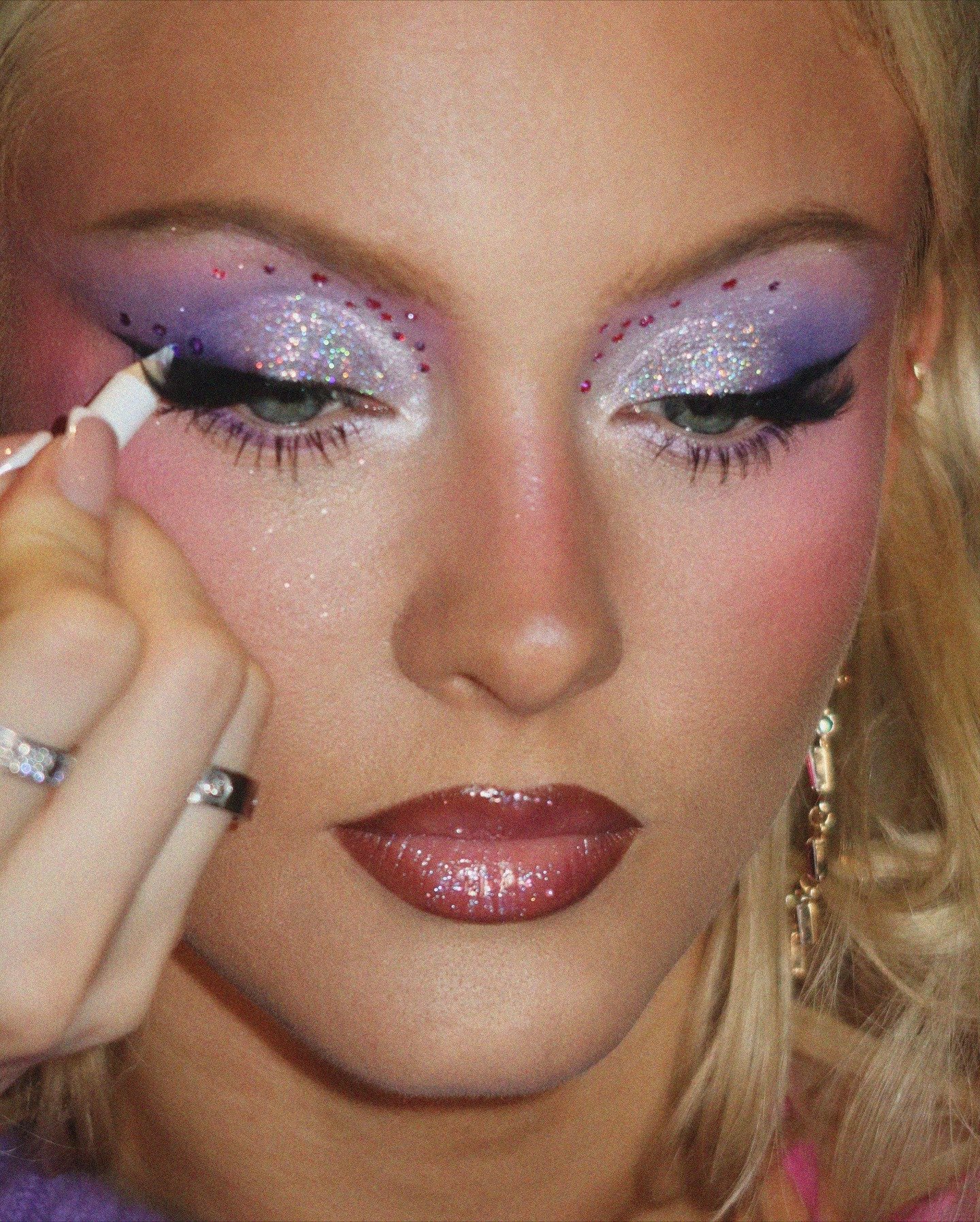 Zara Larsson destaca maquiagem artística com glitter prateado, sombra lilás e rosa, delineado preto e lábios brilhantes