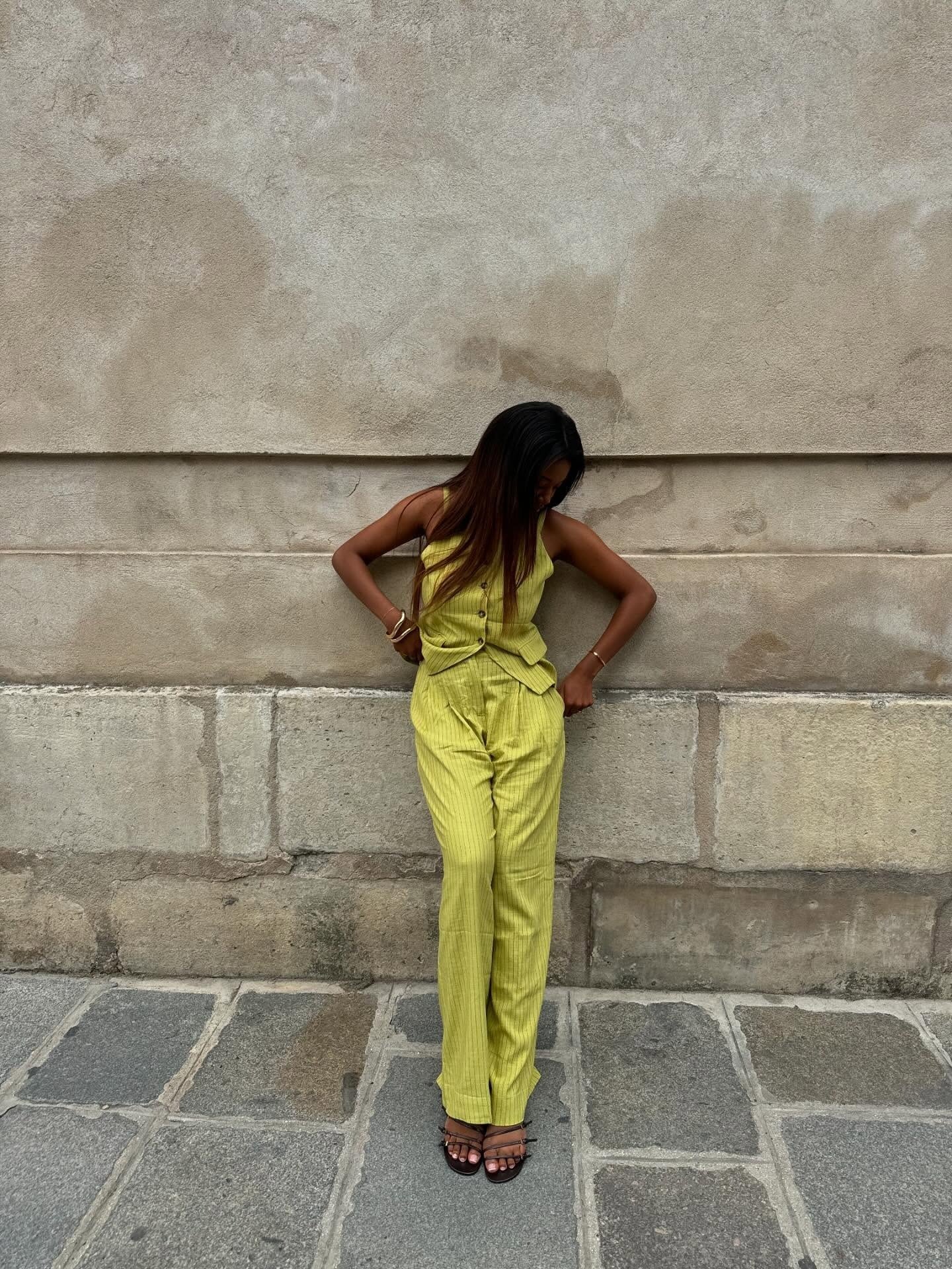 Modelo posa olhando para baixo com postura relaxada, vestindo colete e calça amarelo-limão de linho com riscas finas