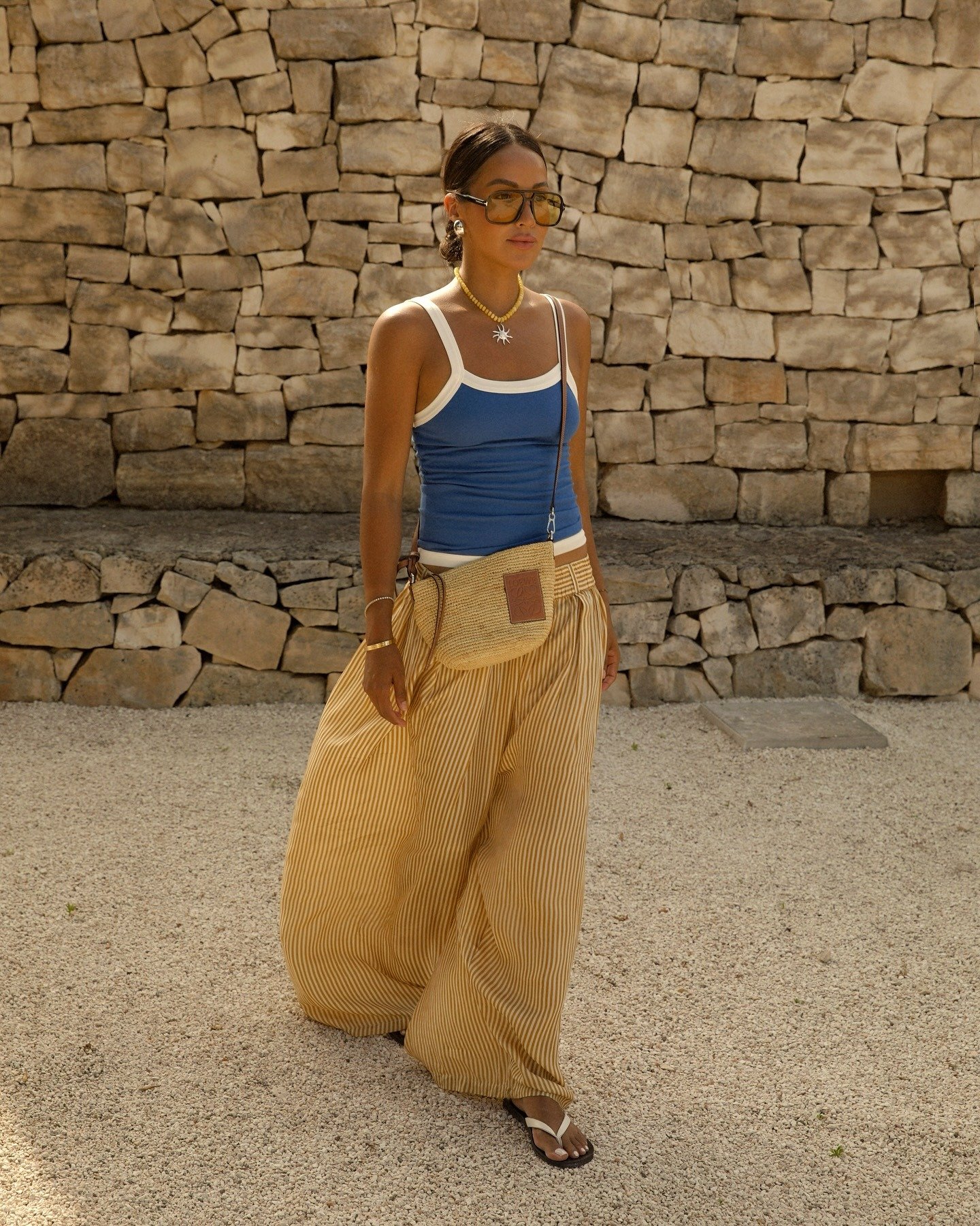 Modelo caminha com looks bonitos em regata azul com detalhes brancos e calça ampla listrada bege, acessórios naturais
