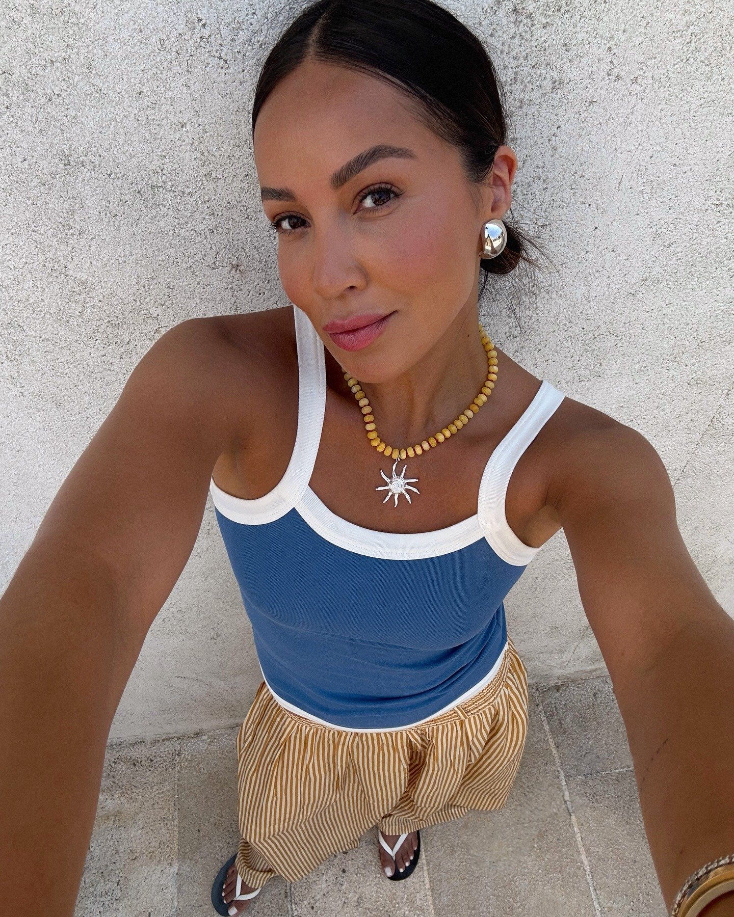 Modelo posa com colar de contas amarelas e pingente de sol prateado, brincos grandes e arredondados, combinando com look