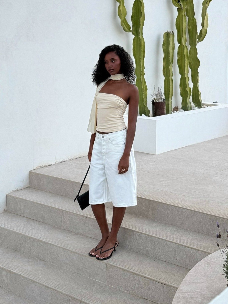 Modelo posa com acessórios tendência de 2026, usando bolsa preta minimalista e sandálias de tiras finas, em look neutro