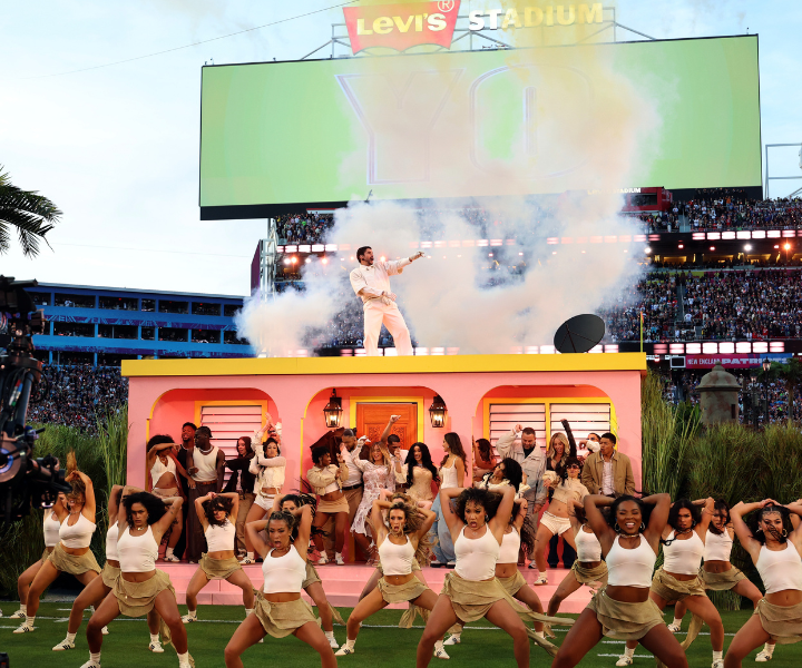 Bad Bunny lidera show vibrante no Levi's Stadium vestindo conjunto branco, cercado por dançarinas em roupas bege e branco.