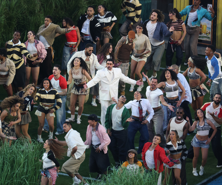 Bad Bunny veste terno branco oversized, rodeado por grupo animado com roupas casuais coloridas e esportivas.