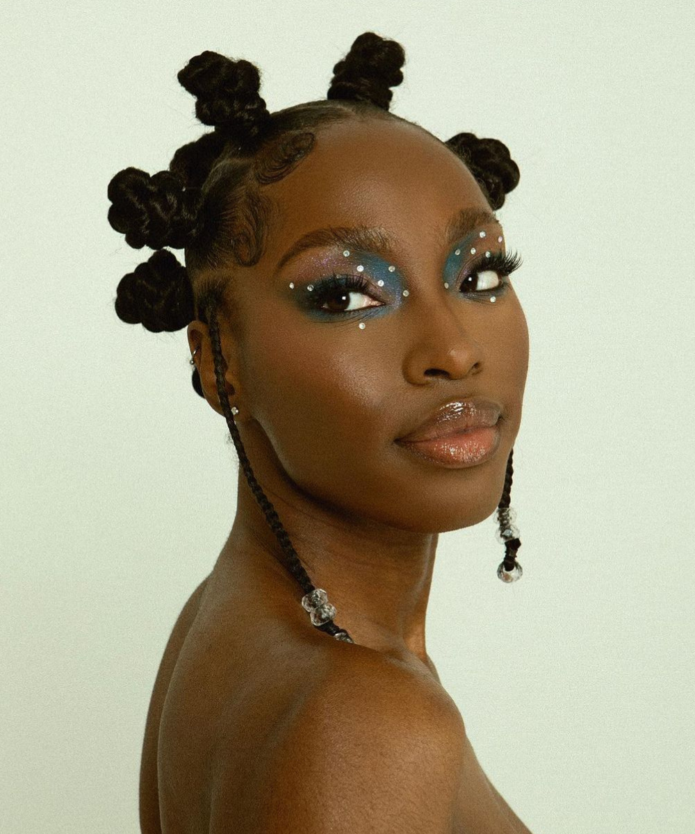 Penteado para Carnaval simples com coques arredondados, tranças com miçangas transparentes e maquiagem azul vibrante com