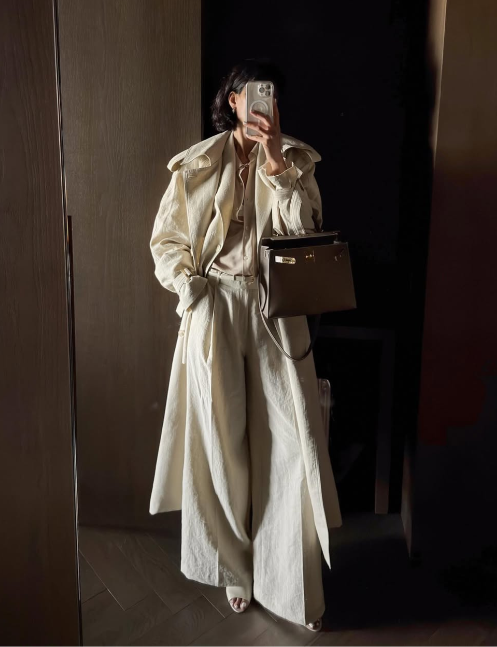 Modelo posa com looks com calça de linho cru ampla, casaco longo texturizado e camisa nude, criando estilo sofisticado.