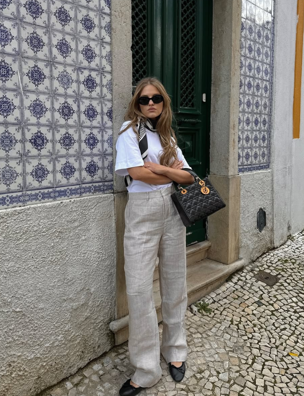 Look com calça de linho cru reta, camiseta branca oversized, lenço preto e branco no pescoço e bolsa preta estruturada.