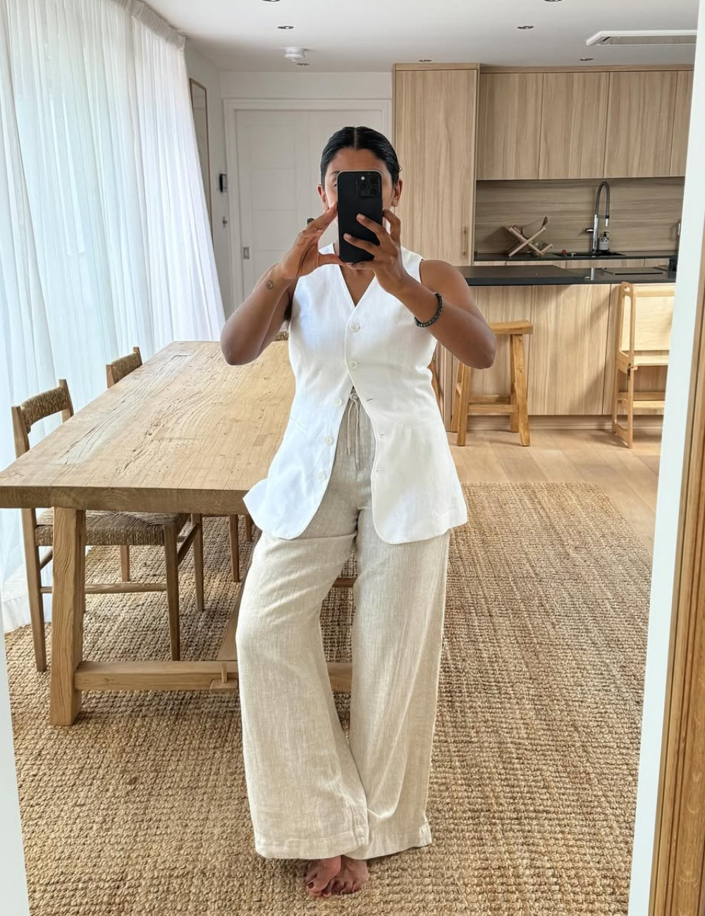 Look com calça de linho cru de modelagem ampla e colete branco estruturado, em ambiente claro e natural.