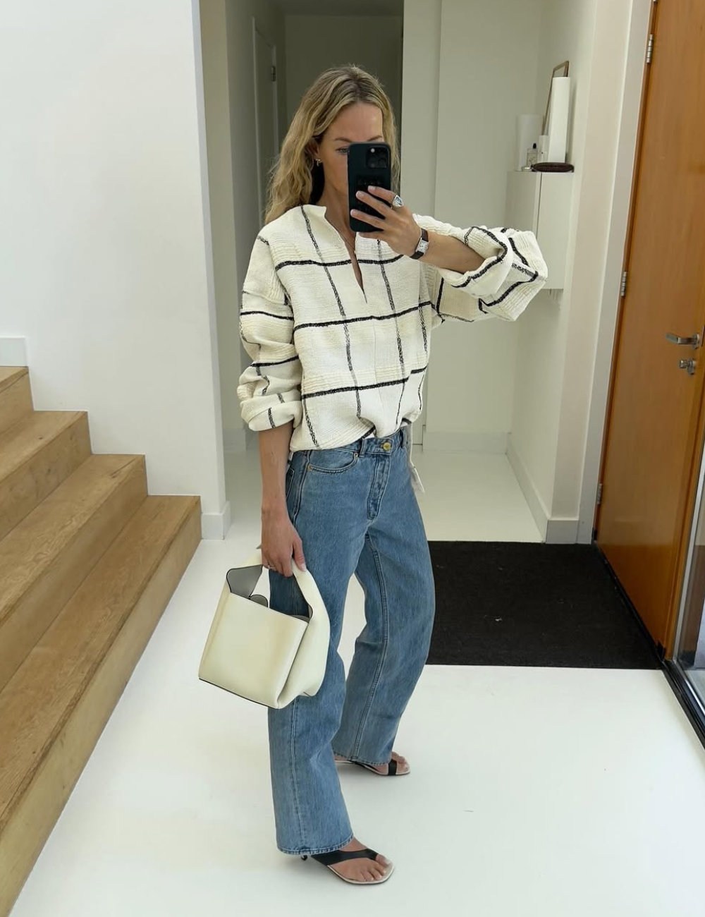 Modelo de calça jeans elegante em lavagem média, corte reto e cintura alta combina com blusa branca de textura.