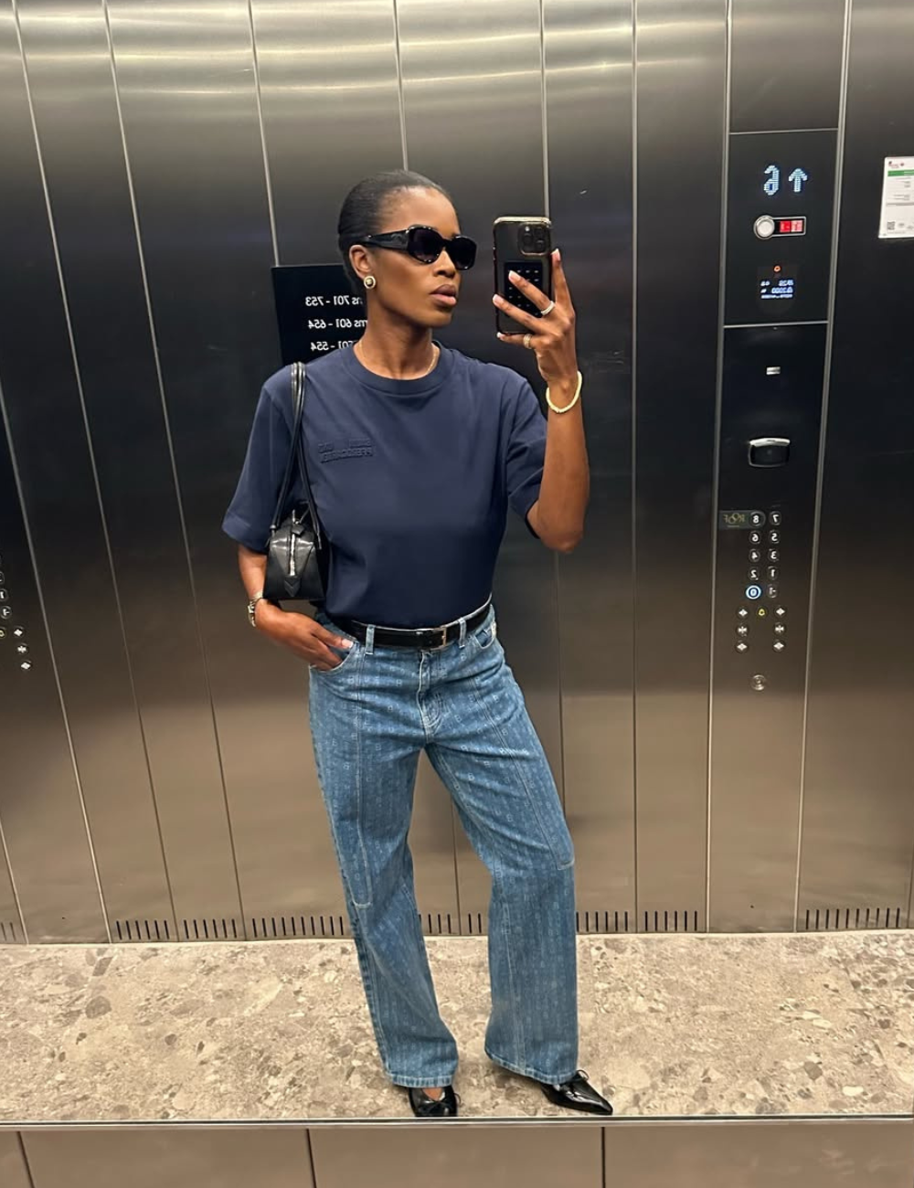 Modelo de calça jeans elegante em lavagem clara com corte reto, combinada a camiseta azul marinho e acessórios pretos.