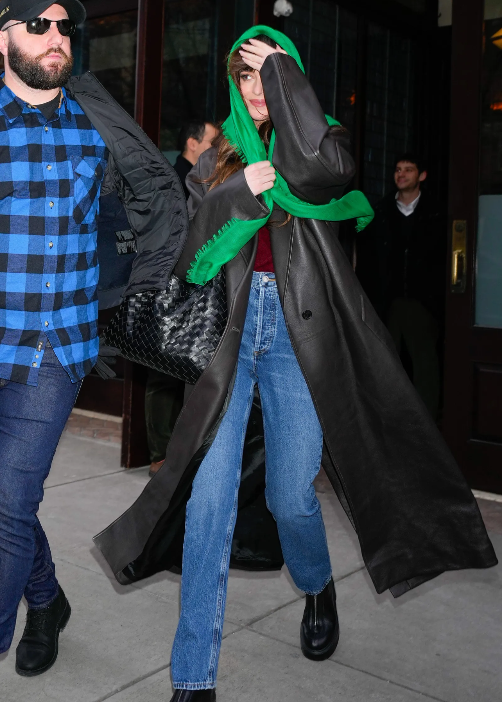 Modelo de calça jeans elegante com corte reto e lavagem média combina com sobretudo preto longo e lenço verde.