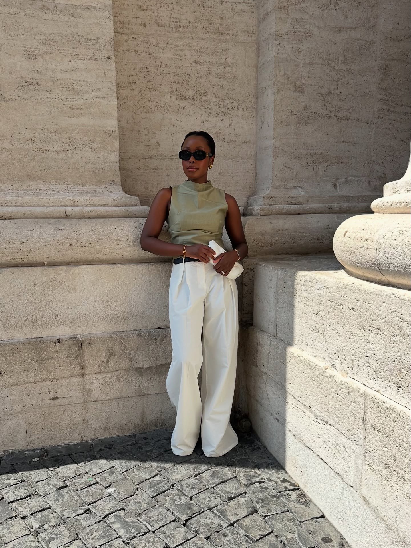 Modelo posa com calça social feminina branca de tecido estruturado e modelagem ampla, combinada a blusa verde oliva