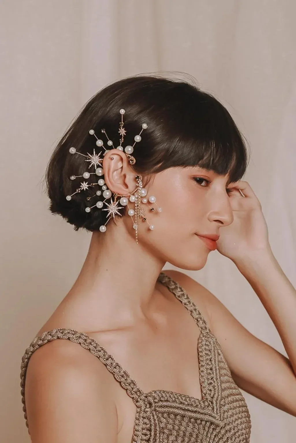 Looks Carnaval 2026 com vestido de crochê bege e acessórios delicados de pérolas e estrelas, modelo posa com expressão