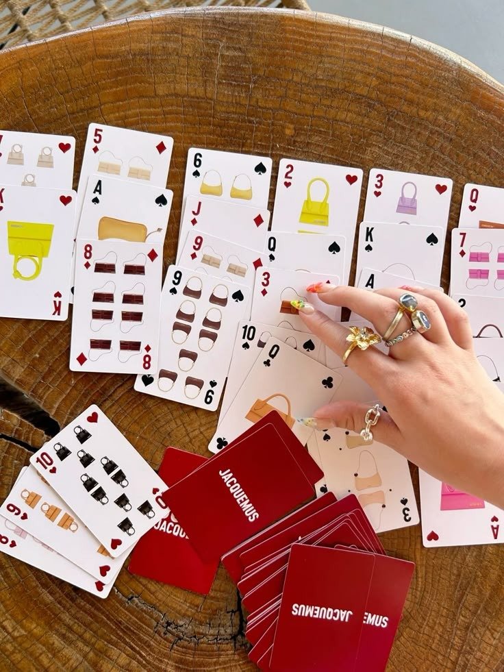 Mão com anéis delicados manuseia cartas de baralho personalizadas com bolsas coloridas em tons terrosos e vibrantes