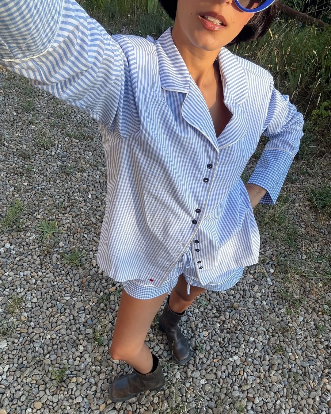 Modelo posa com short soltinho xadrez azul claro e branco, combinando com camisa listrada oversized e botas pretas, em