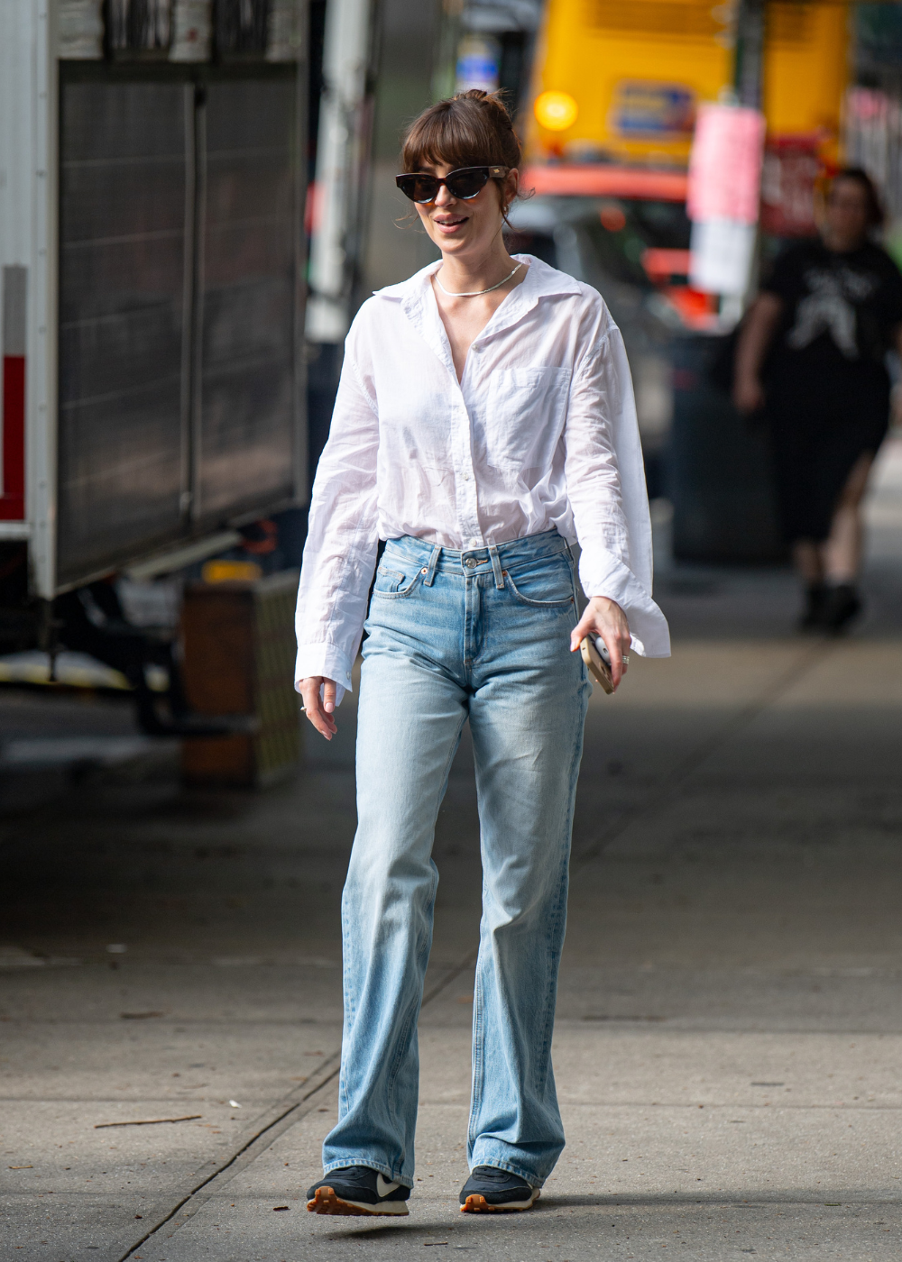 Mulher caminha confiante usando tênis da moda de 2026 em preto com sola marrom, combinando com jeans claro e camisa branca.