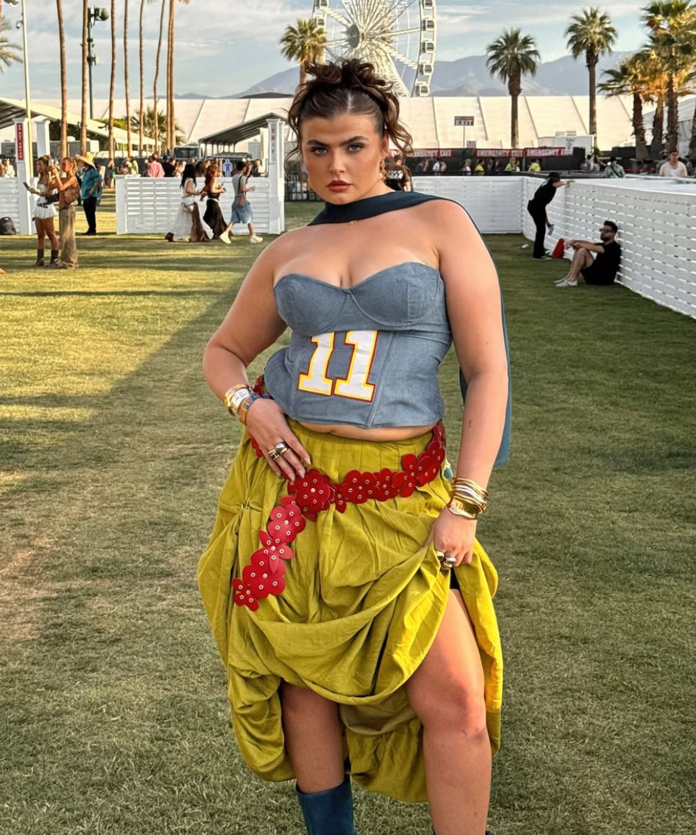 Modelo posa confiante com top tomara que caia jeans azul, saia amarelo mostarda drapeada e cinto Y2K vermelho de flores.