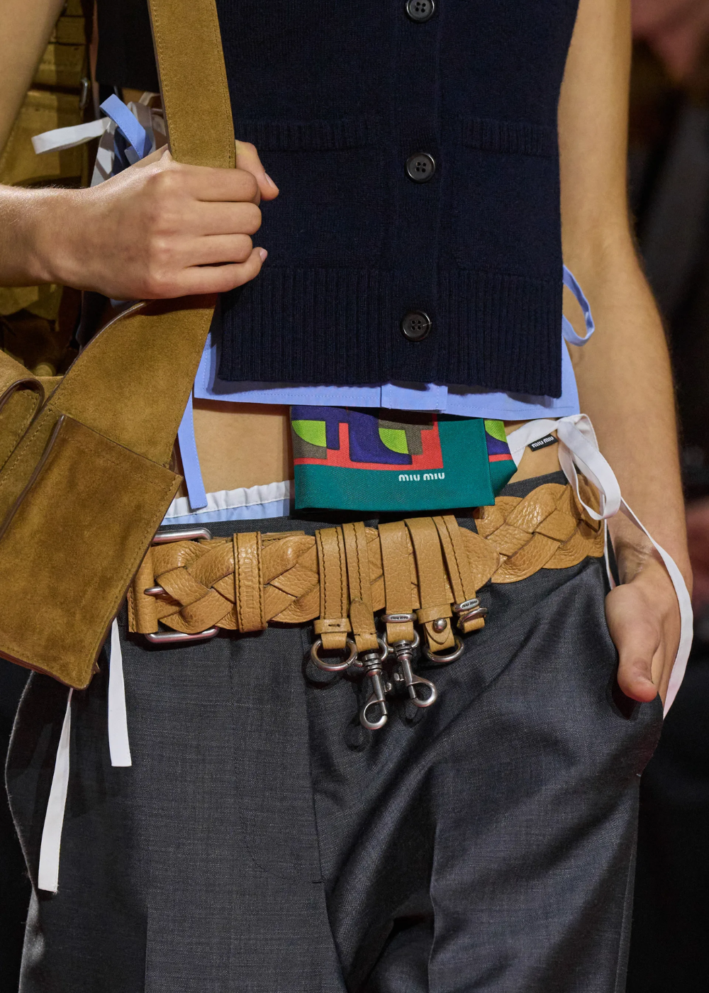 Cinto Y2K em couro caramelo trançado com fivelas e ganchos metálicos, combinado a colete preto e calça cinza.