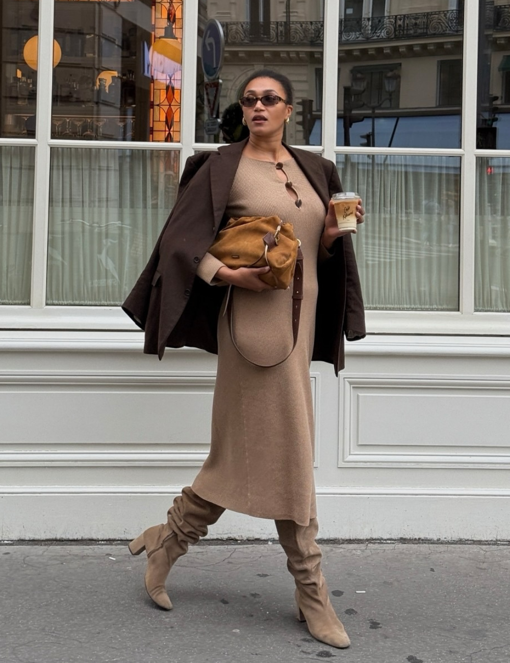 Modelo caminha confiante usando vestido midi de tricô bege com botas de cano alto e blazer marrom, combinando bolsa caramelo.