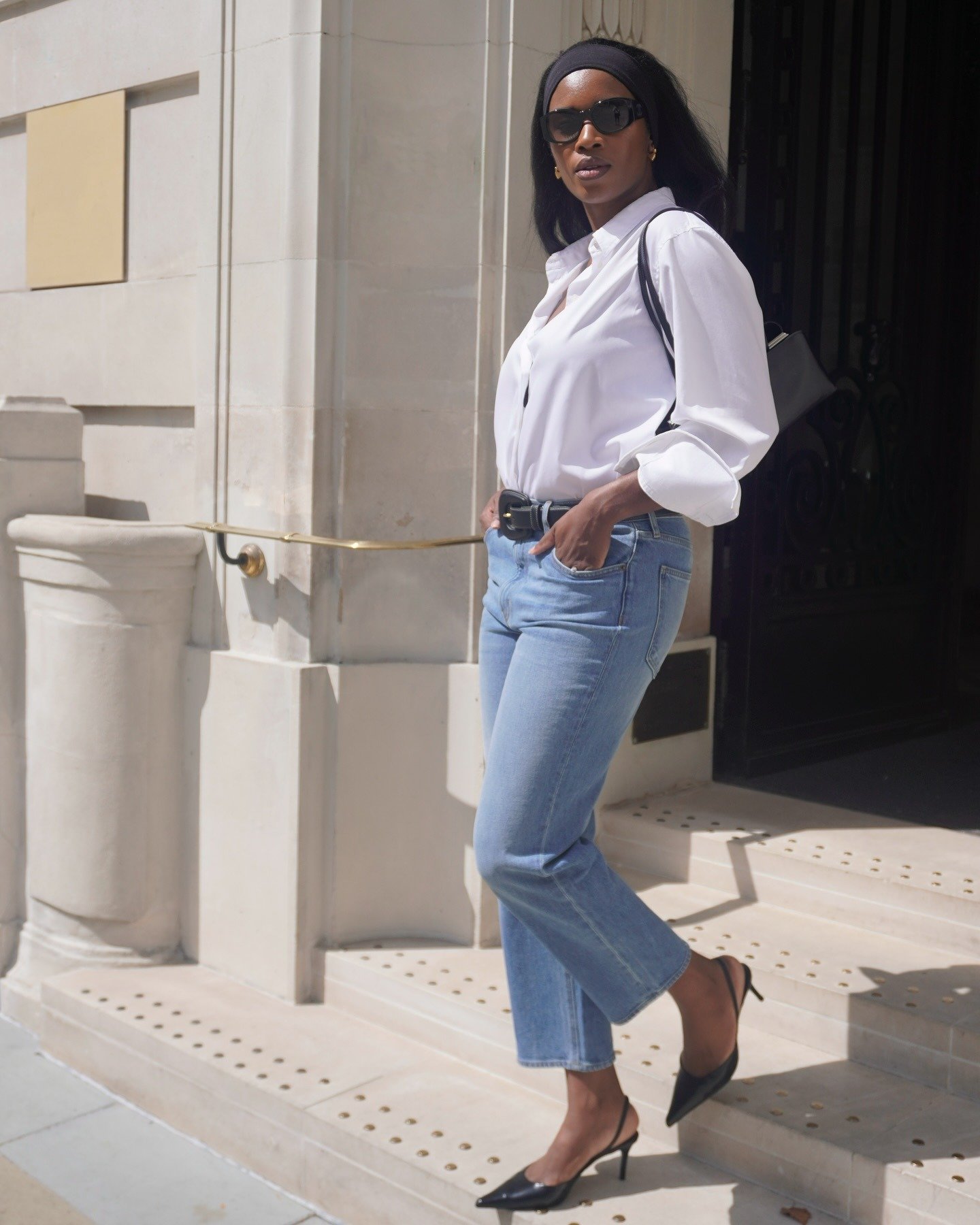 Mulher posa com camisa branca de algodão, calça jeans azul clara reta, cinto preto e scarpin, combinando elegância