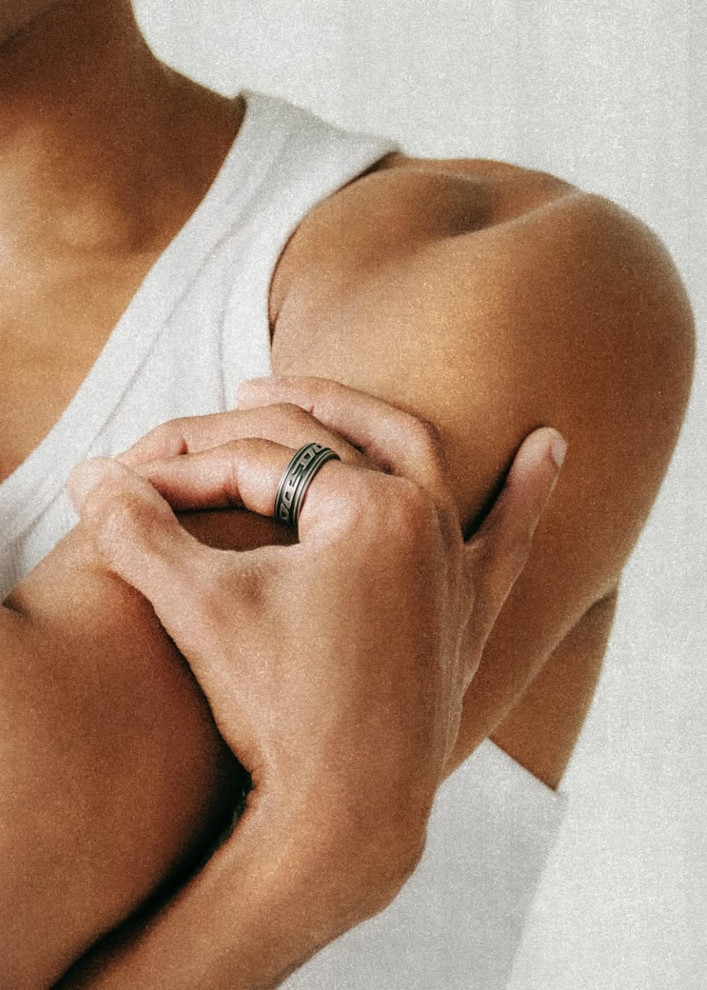 Mão com anel wearables de metal escovado com design geométrico segura braço vestido com regata branca.