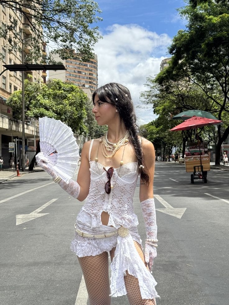 Fantasia de carnaval em renda branca com corpete, saia curta, luvas e acessórios de pérolas, modelo posa elegante com leque