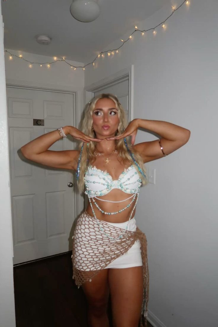 Fantasia de carnaval com top branco adornado por pérolas azuis, saia curta branca e rede bege, modelo posa alegre