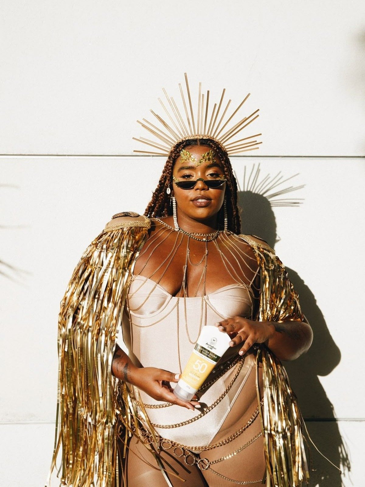 Fantasia de carnaval dourada com body estruturado, franjas metálicas, correntes e adereço de raios, modelo posa confiante