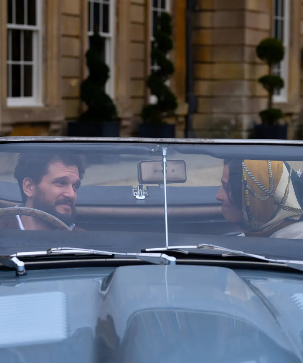 Cena da quarta temporada de Industry mostra homem com blazer marrom e mulher com lenço estampado em tom mostarda, num carro