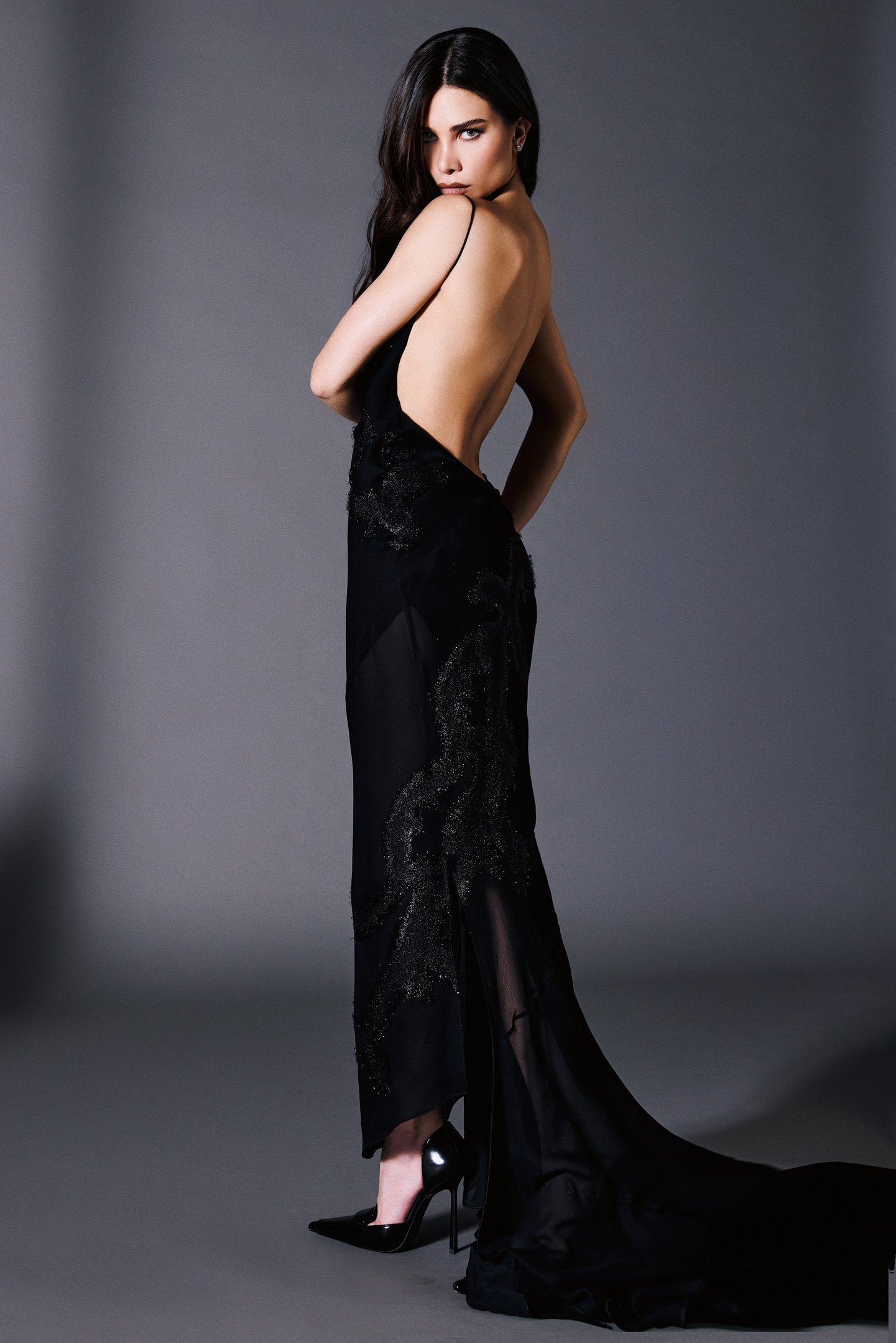 Flávia Pavanelli posa com vestido preto longo de tecido fluido e detalhes texturizados, decote nas costas e salto alto, em