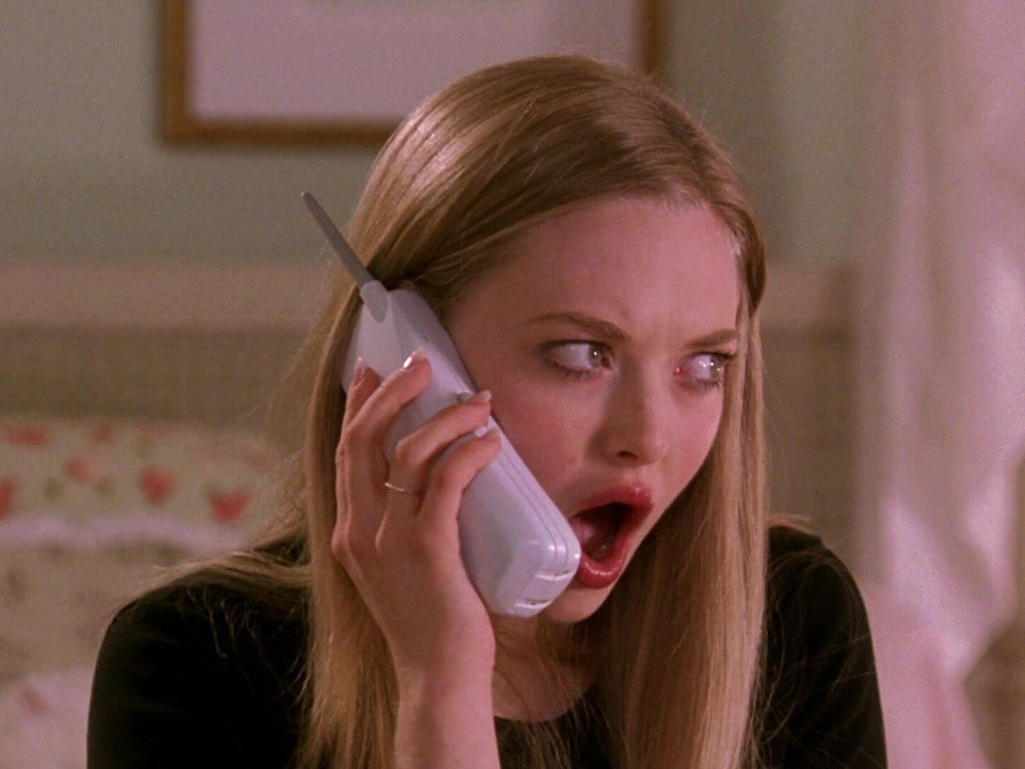 Mulher loira com blusa preta, cabelo liso e maquiagem natural expressa choque. Fofoca nos relacionamentos