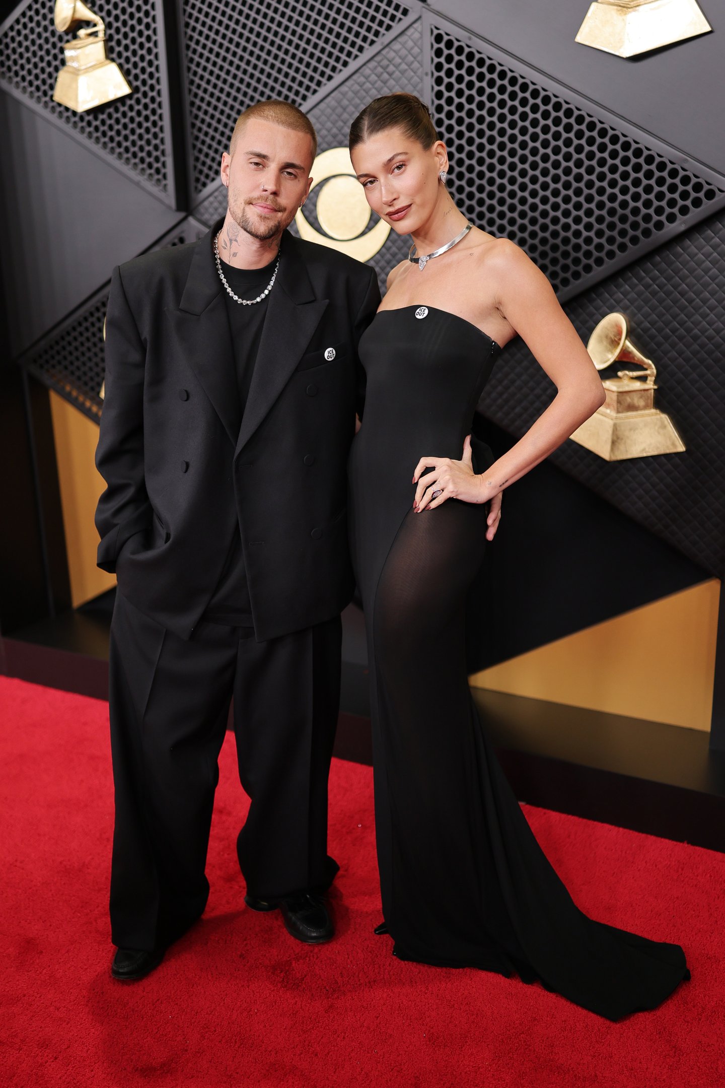 Casal posa no Grammy 2026 com looks pretos: blazer oversized e calça larga em tecido fosco, vestido longo justo com