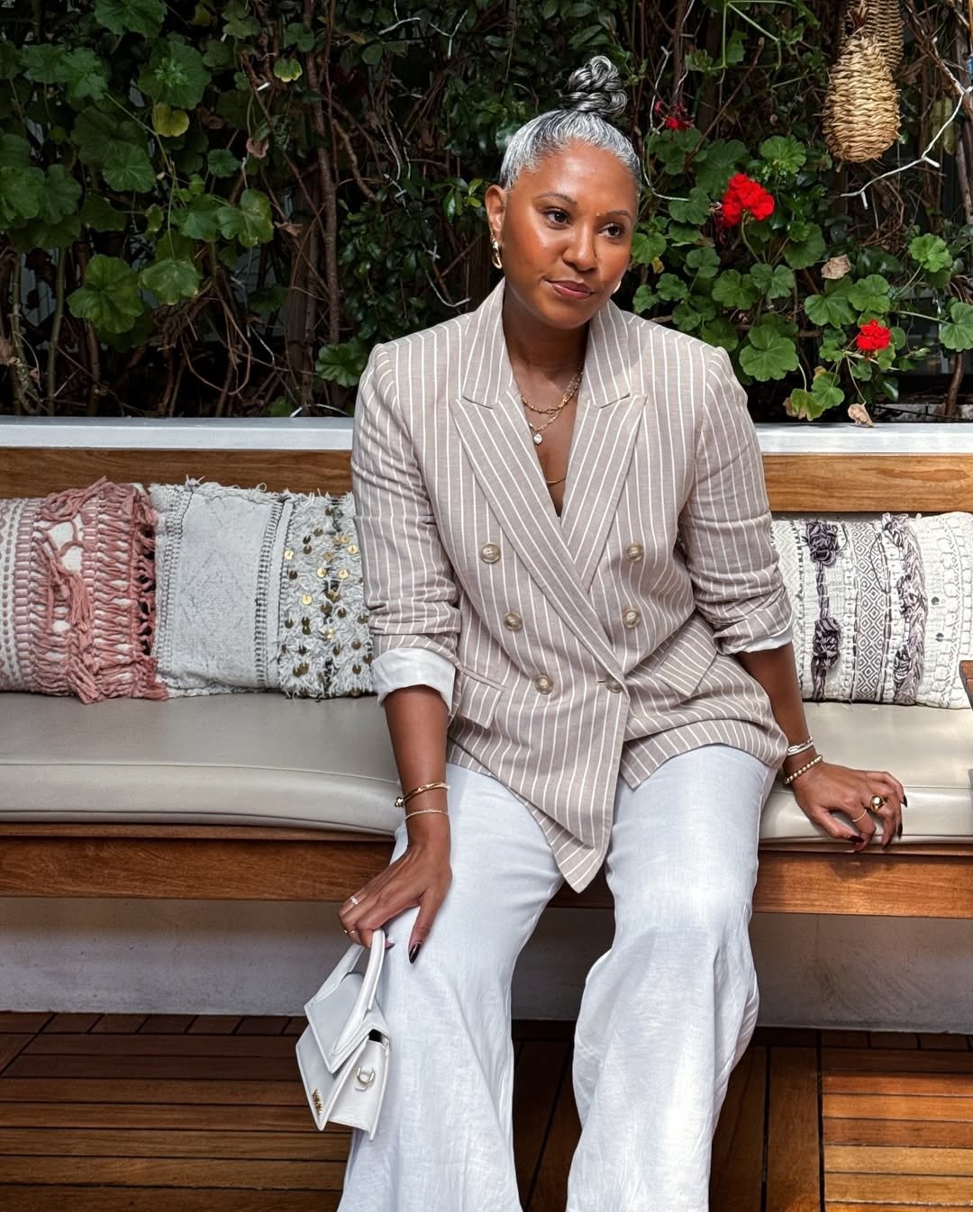 Mulher posa sentada com blazer listrado bege e calça  - representando o melhor hidratante para pele madura