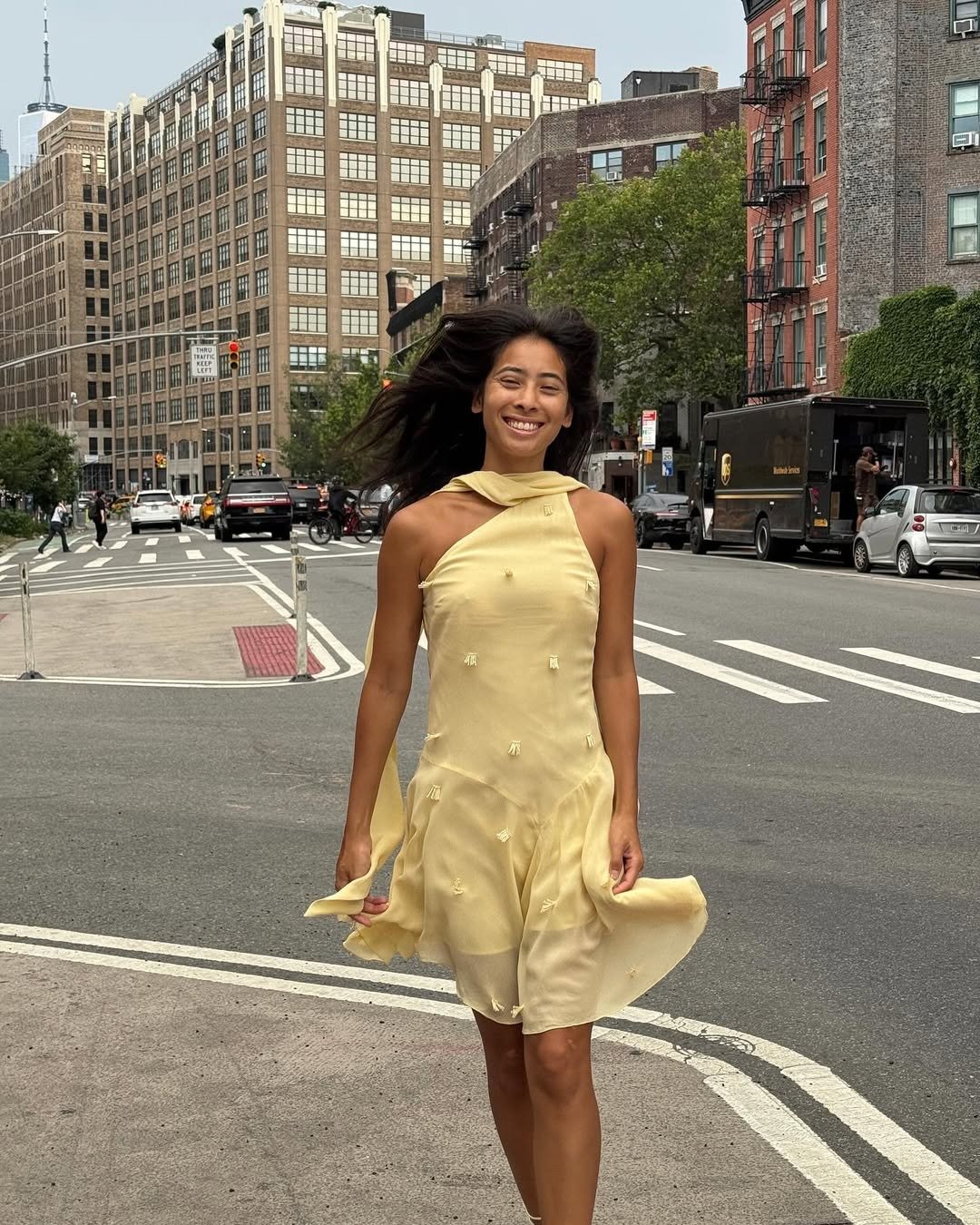 Modelo caminha sorridente em vestido de verão chique amarelo claro com tecido leve, detalhes bordados e corte assimétrico