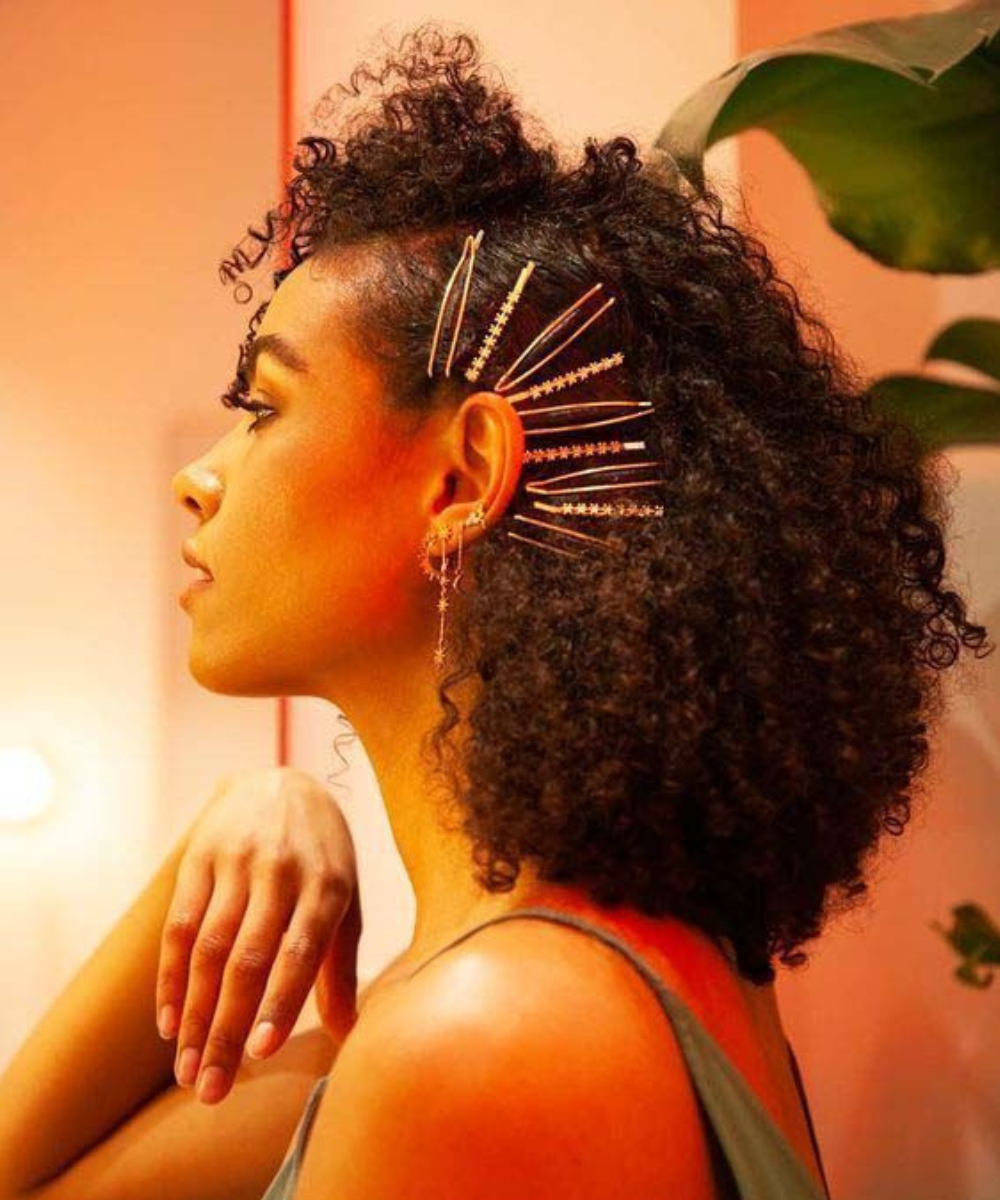 Penteado para Carnaval simples com cabelo cacheado solto e presilhas douradas decorativas, clima descontraído e elegante.