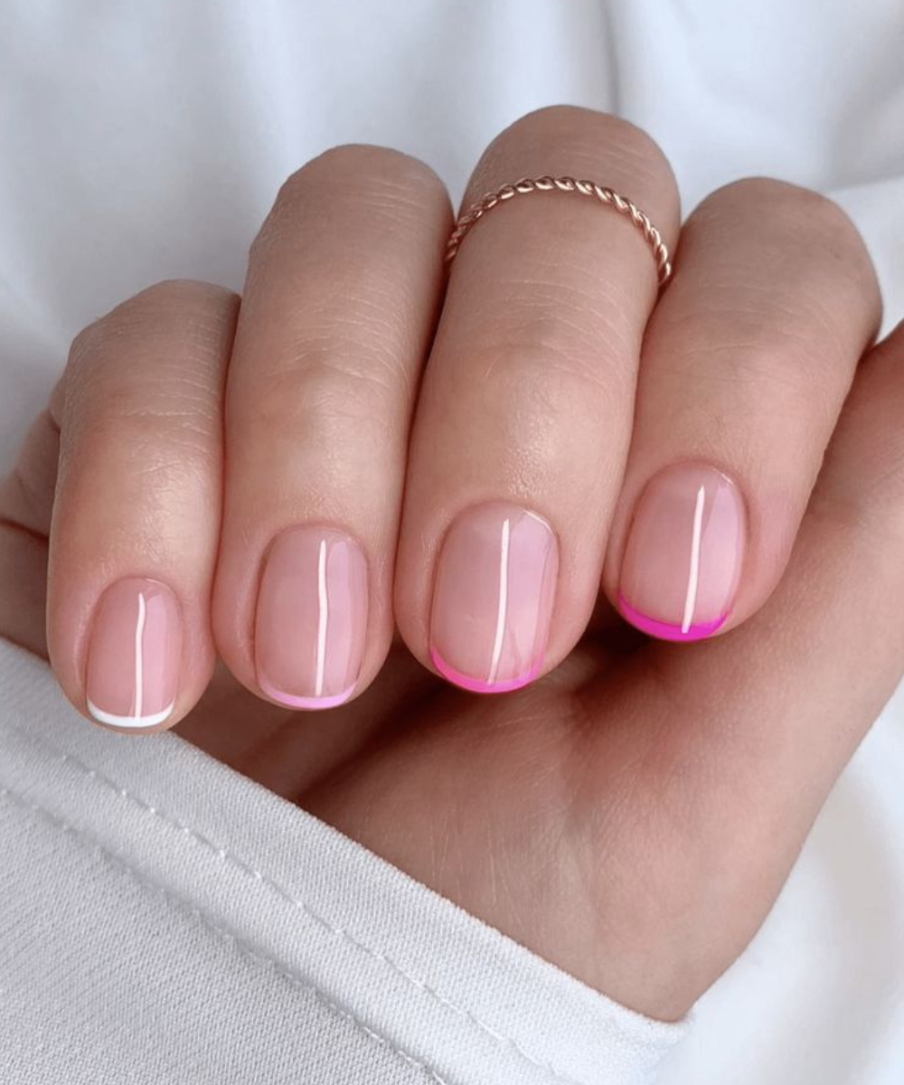 Unhas minimalistas com base nude e pontas finas em branco e tons de rosa vibrante, destacando delicadeza e modernidade.