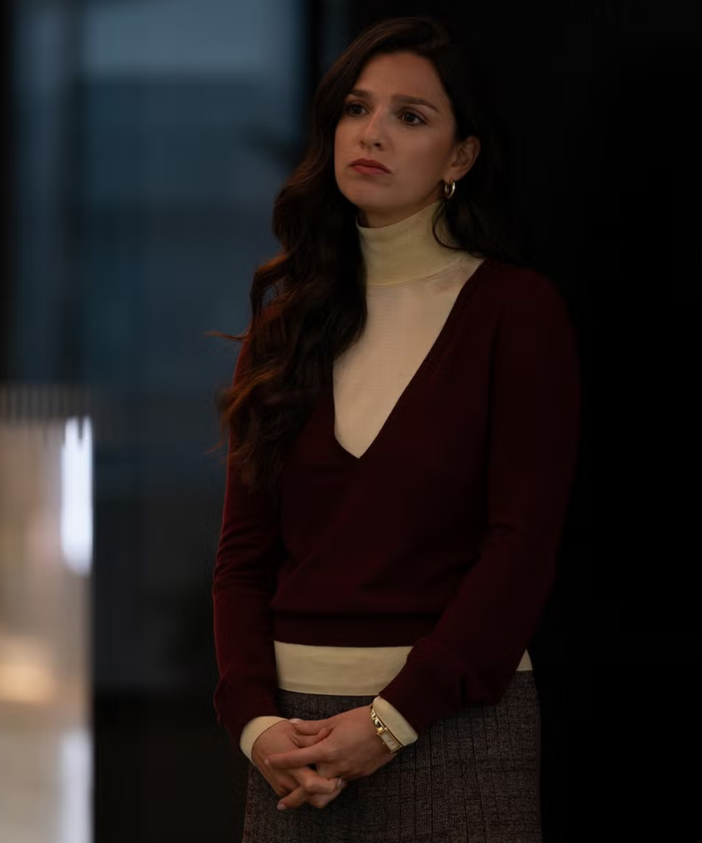 Mulher na quarta temporada de Industry veste blusa vinho com decote em V sobre gola alta creme, saia cinza texturizada,