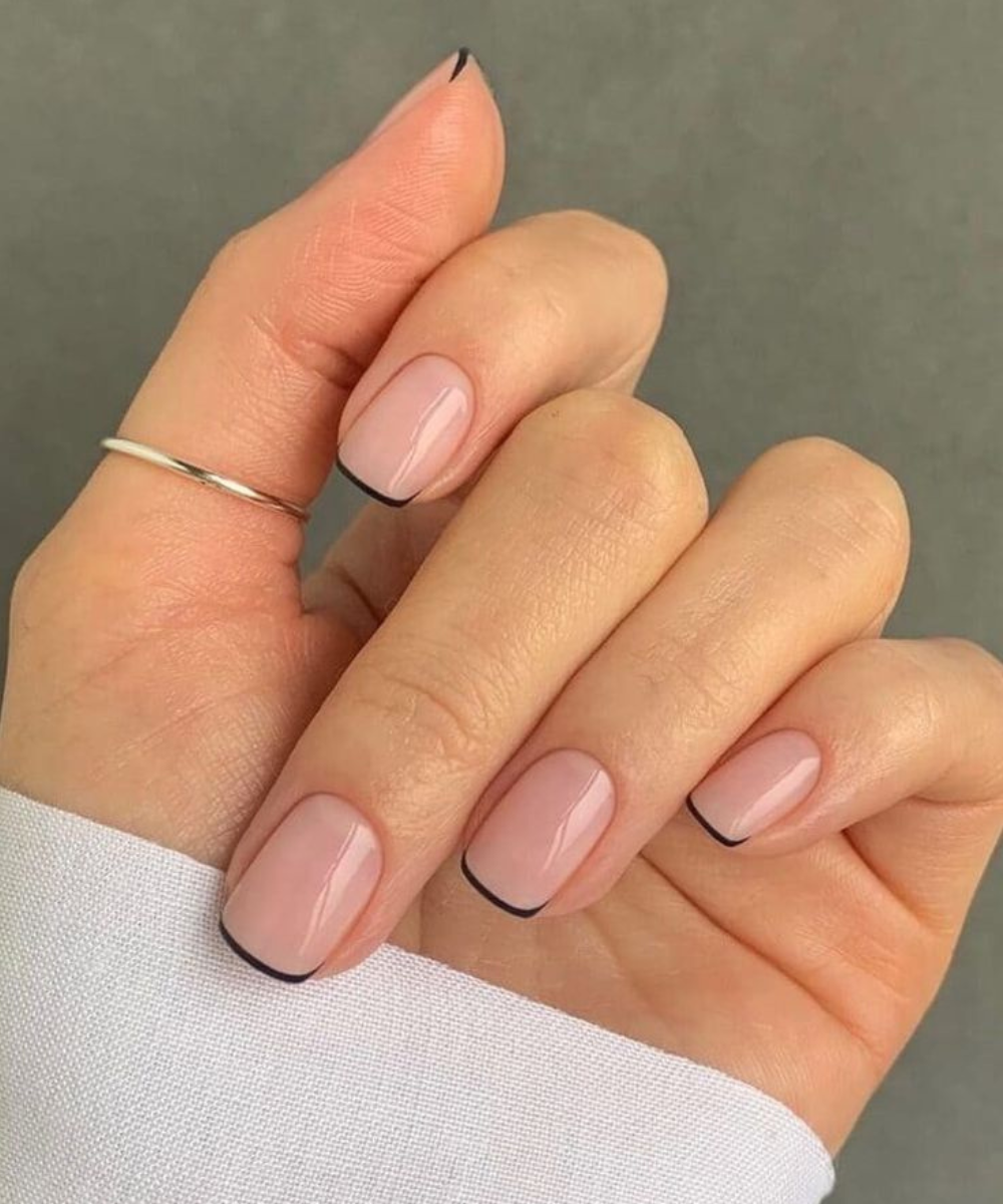 Unhas minimalistas com base nude e delicada borda preta na ponta destacam a elegância sutil e moderna da tendência de unhas