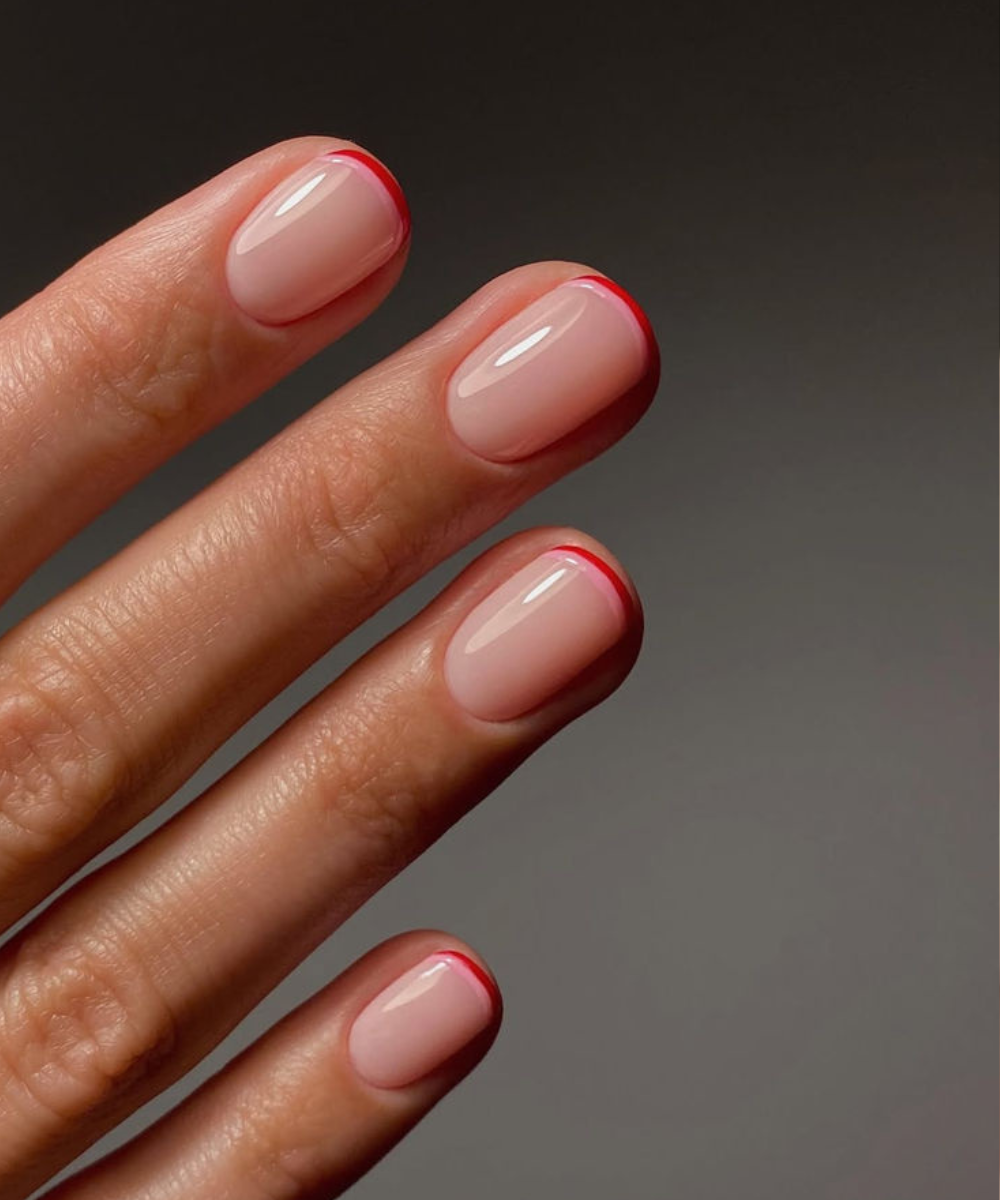 Unhas minimalistas com base nude e pontas finas em vermelho vibrante destacam elegância sutil e modernidade na tendência de