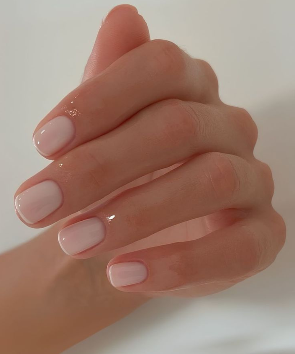 Tendência de Unhas minimalistas com esmalte nude perolado em formato curto e arredondado, realçando delicadeza.