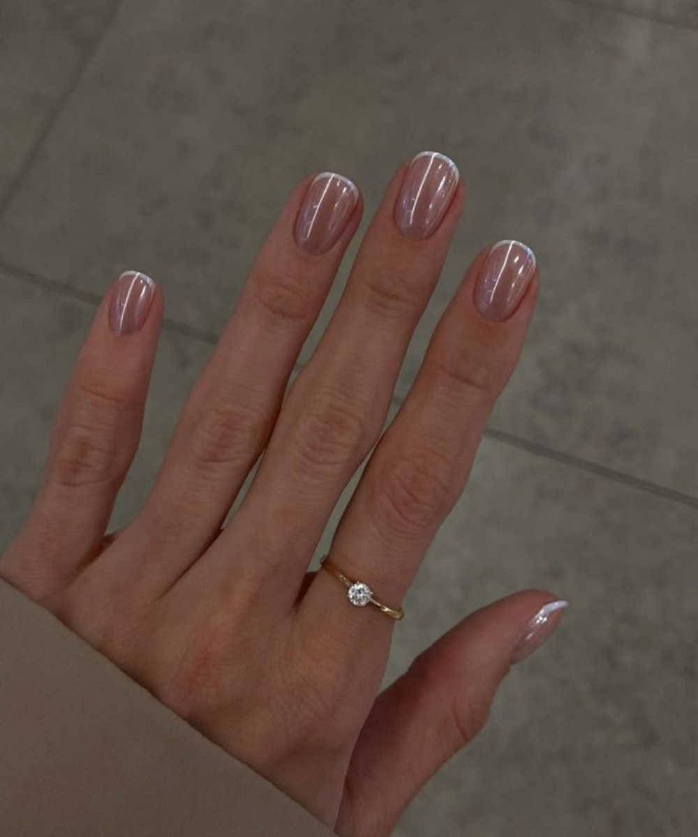 Unhas minimalistas com base nude e ponta branca delicada realçam elegância sutil, acompanhadas por anel dourado com pedra