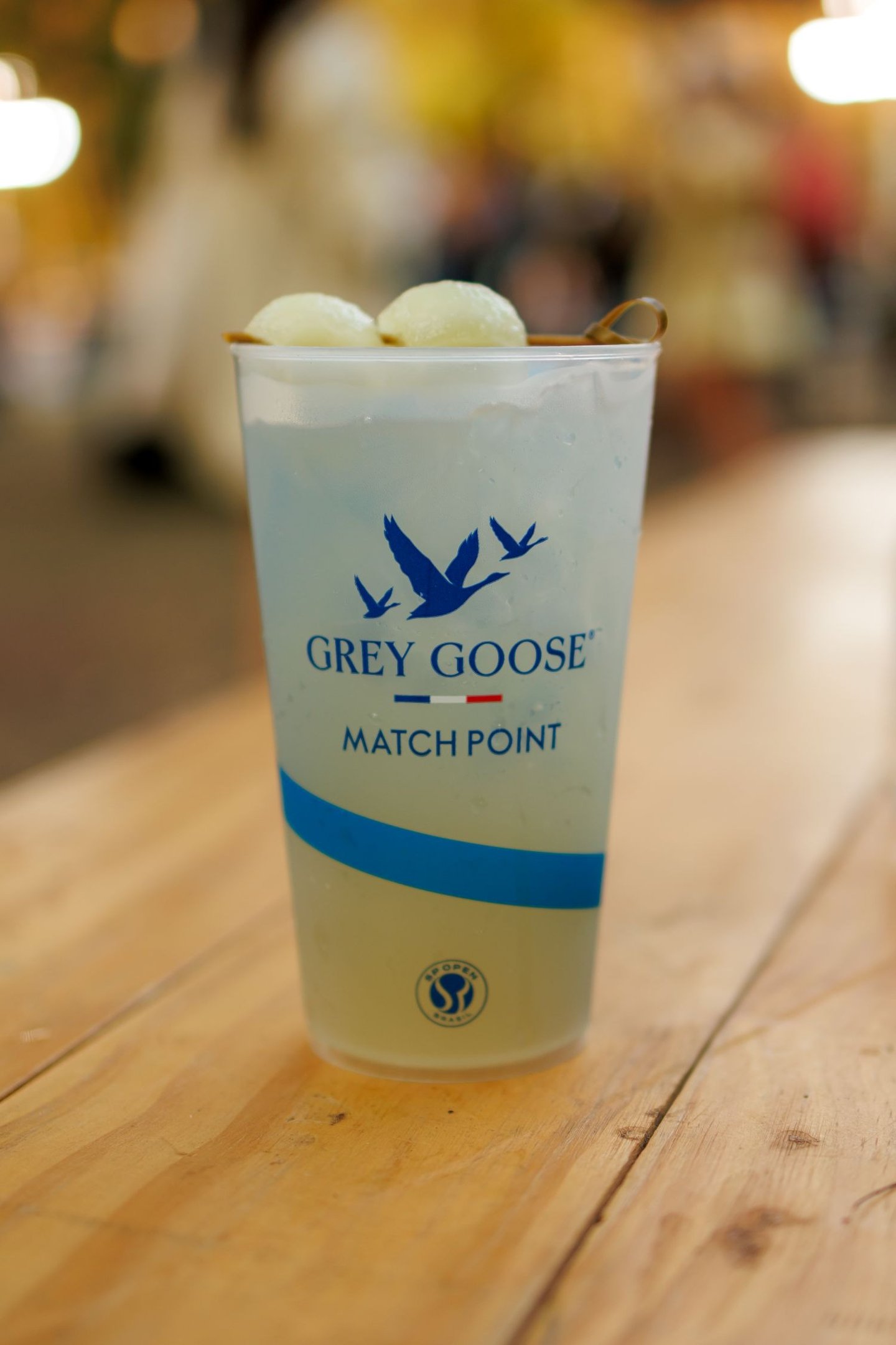 Copo transparente com drink gelado e gelo, detalhes em azul e branco, sobre mesa de madeira clara em clima descontraído no