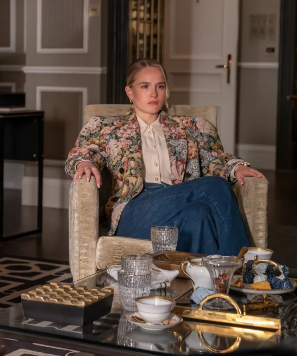 Na quarta temporada de Industry, modelo posa com blazer floral estruturado, camisa de botões perolados e jeans azul, em