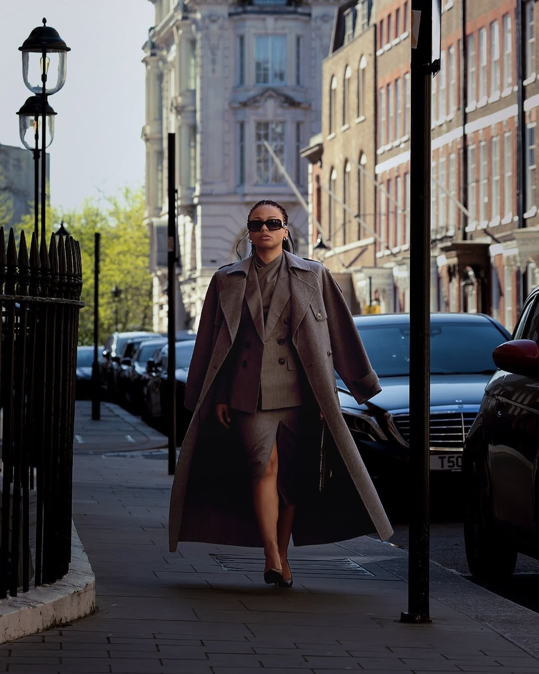Mulher caminha confiante em rua urbana usando sobretudo cinza longo, blazer e saia com fenda, estilo elegante na quarta