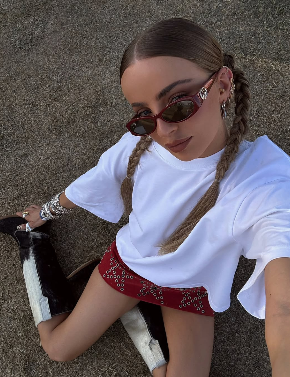 Look para o show do Bad Bunny com camiseta branca oversized, minissaia vermelha com ilhós metálicos, botas de couro bicolor.