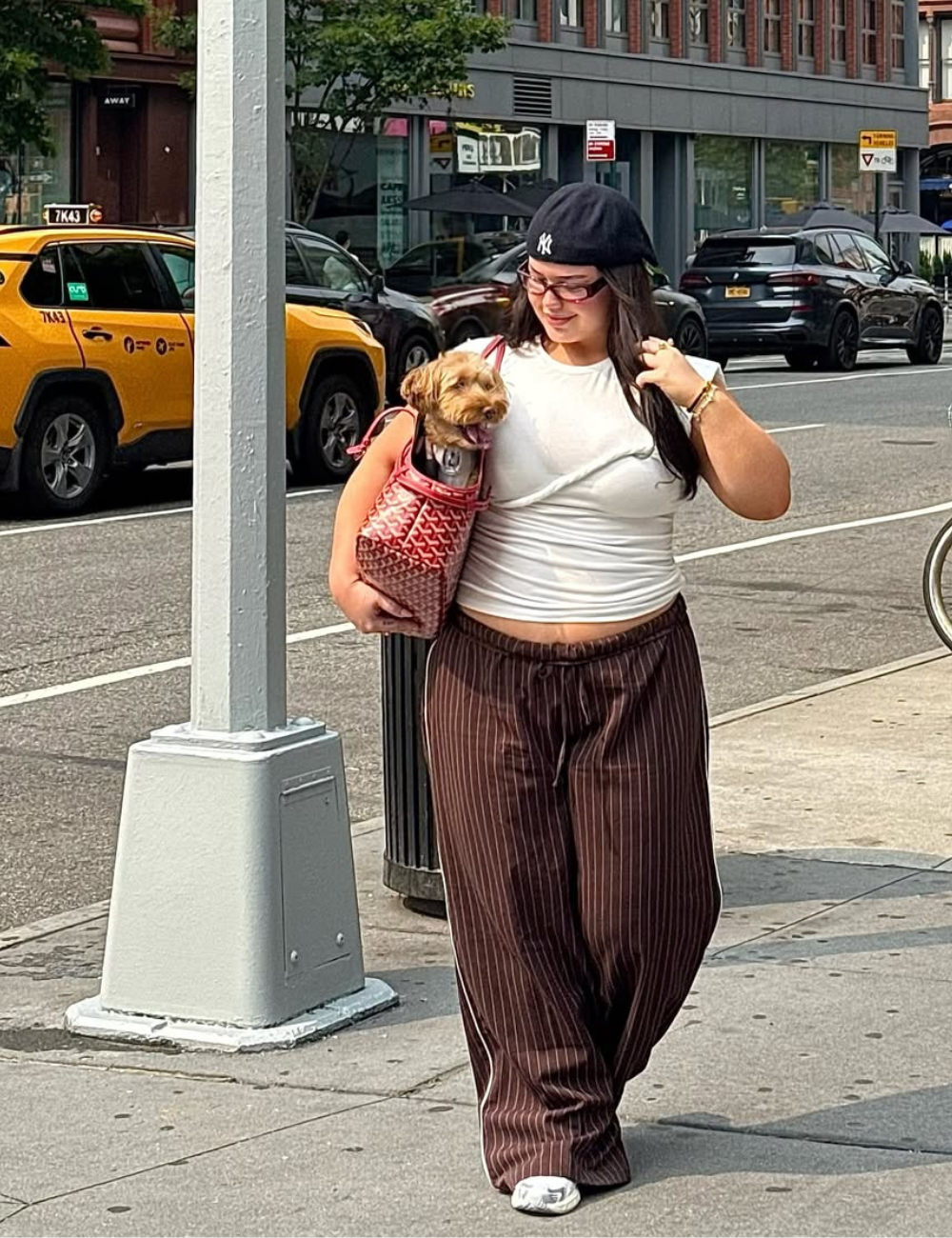 Look para o show do Bad Bunny com calça larga marrom listrada, camiseta branca justa, boné preto e bolsa vermelha estilosa.